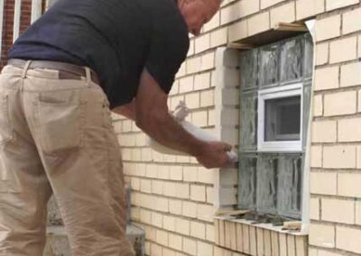 Glass Block Window Installers - Photo of a man installing a glass block window using a concrete mortar bag to fill the joints around the window.