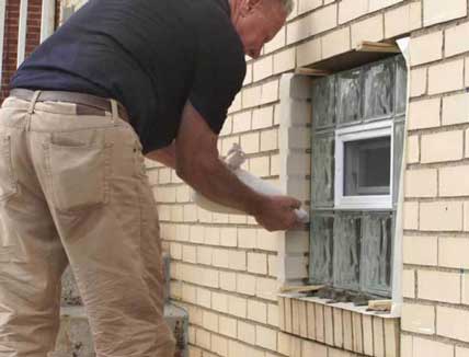 Glass Block Window Installers - Photo of a man installing a glass block window using a concrete mortar bag to fill the joints around the window.